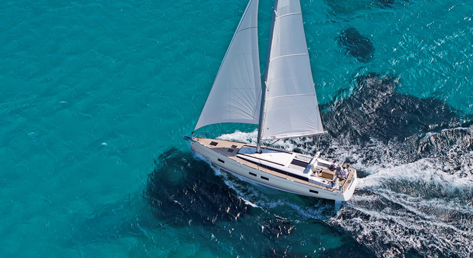A Beneteau sailing yacht under full sail in bright turquoise water, seen from above