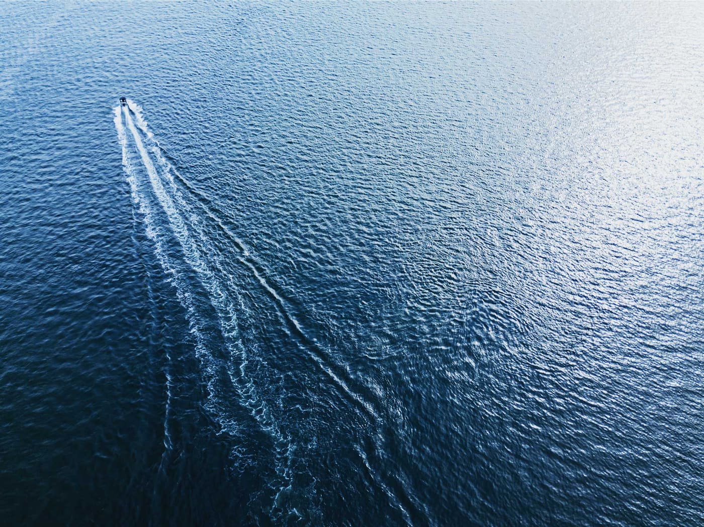 Aerial view of a motorboat carving a long white wake across open blue water
